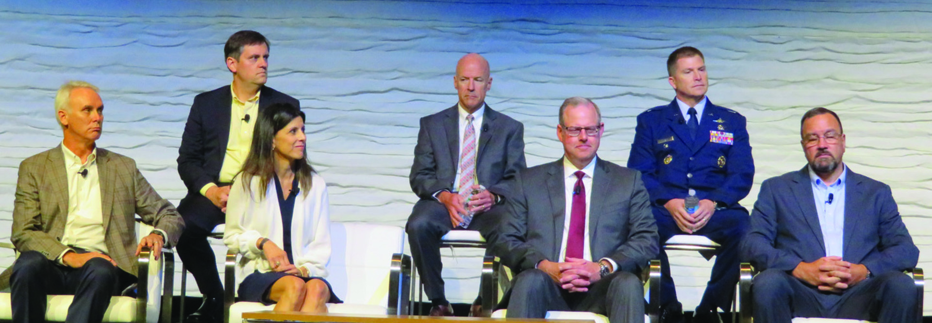 Two rows of people, three men at the top, one man, one woman and two men at the bottom, all in business wear